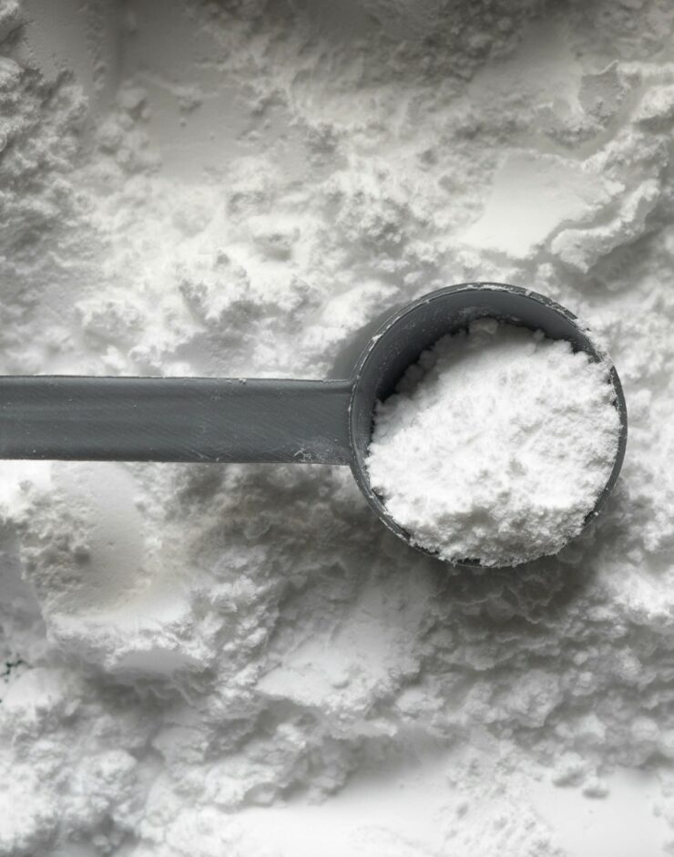 Scoop of maltodextrin powder lawing on a background of maltodextrin powder.