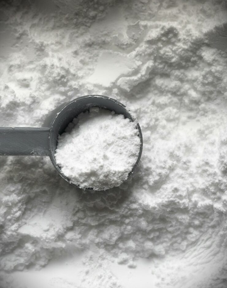 Scoop of polydextrose powder lawing on a background of polydextrose powder.