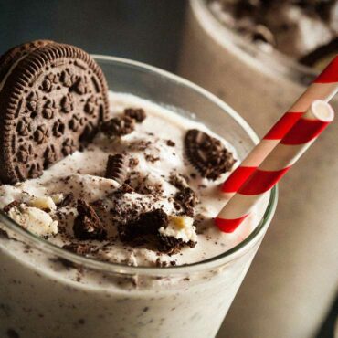 Chocolate milkshake with a chocolate biscuit in it and a white and red straw.