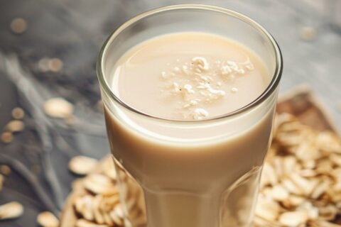 A glass on oat milk surrounded by scattered oats.