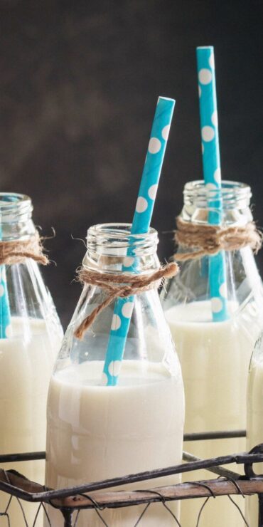 Glass bottles of vegan milk with straws next to various nuts.