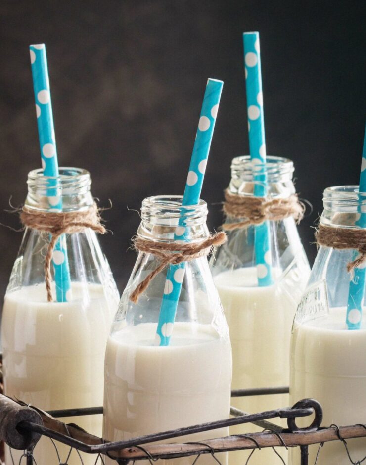 Glass bottles of vegan milk with straws next to various nuts.