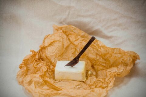 Vegan butter on unwrapped paper with a wooden knife in it.
