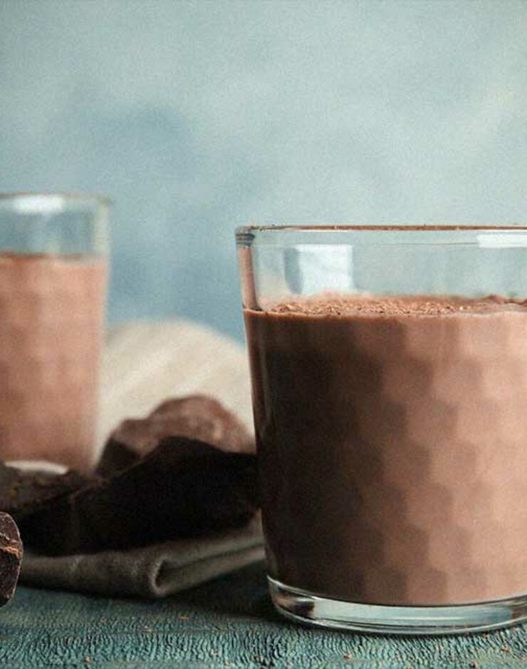Two glasses of chocolate milk on a table next to blocks of chocolate.