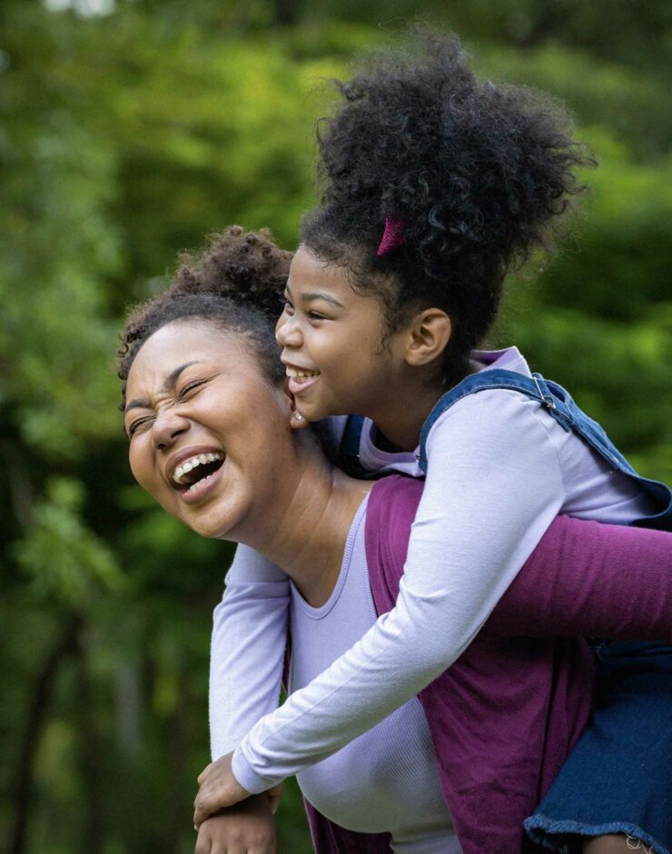 Mother laughing whilst giving her daughter a piggyback.