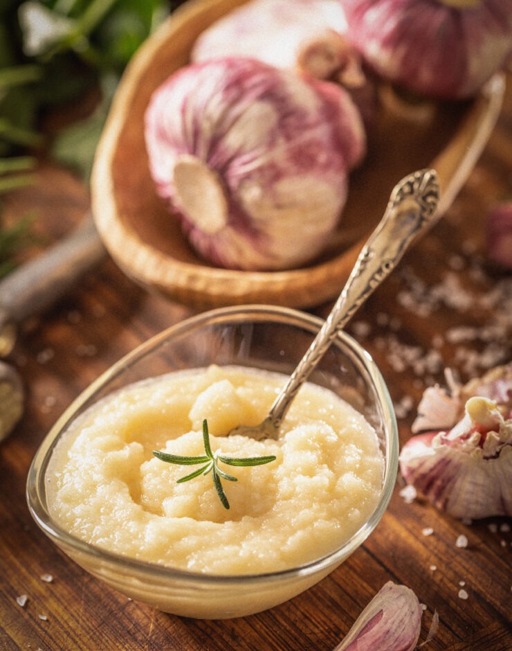 Garlic puree in a glass dish with garlic bulbs in the background.