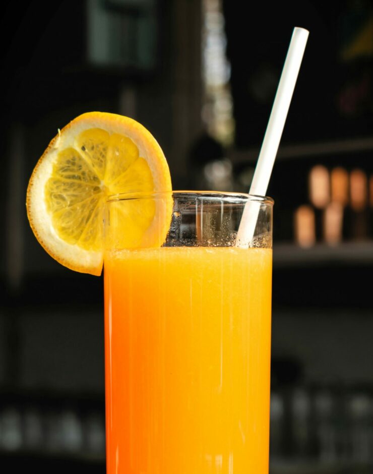 Tall glass of orange juice with a a straw and slice of orange.