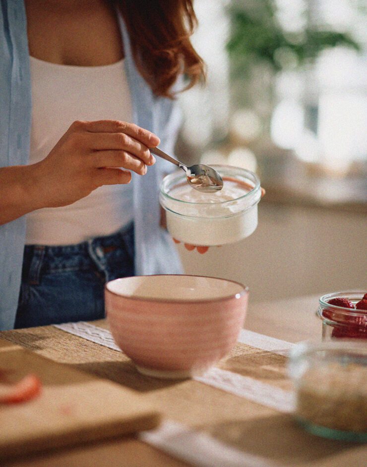 Lady spooning yoghurt into a bowl with fruit.
