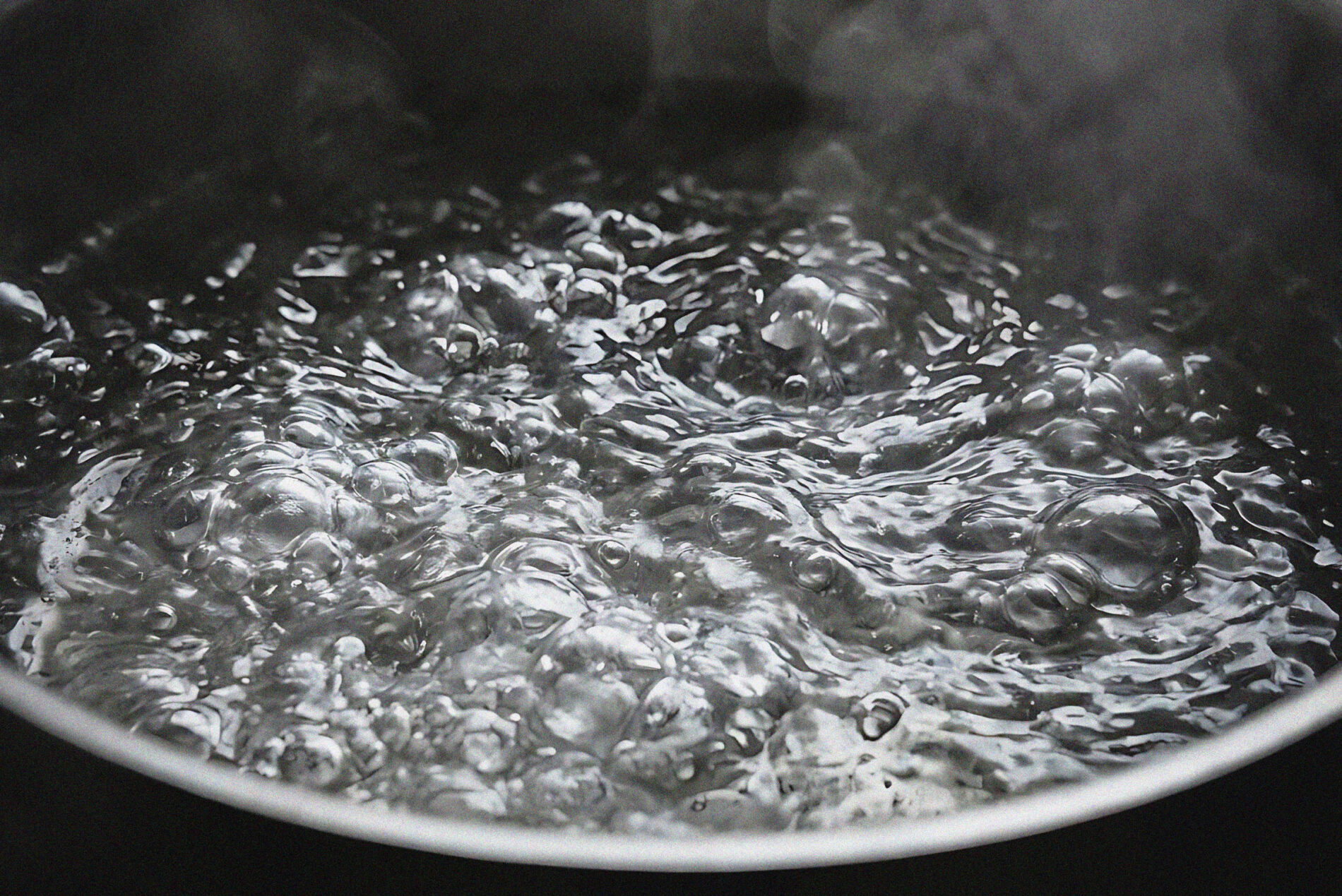 Close-up of water vigorously boiling in a saucepan, with large bubbles and steam rising from the surface.