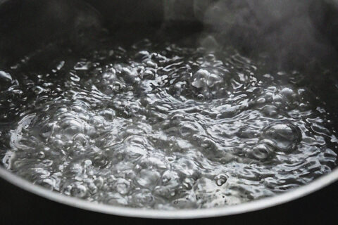 Close-up of water vigorously boiling in a saucepan, with large bubbles and steam rising from the surface.